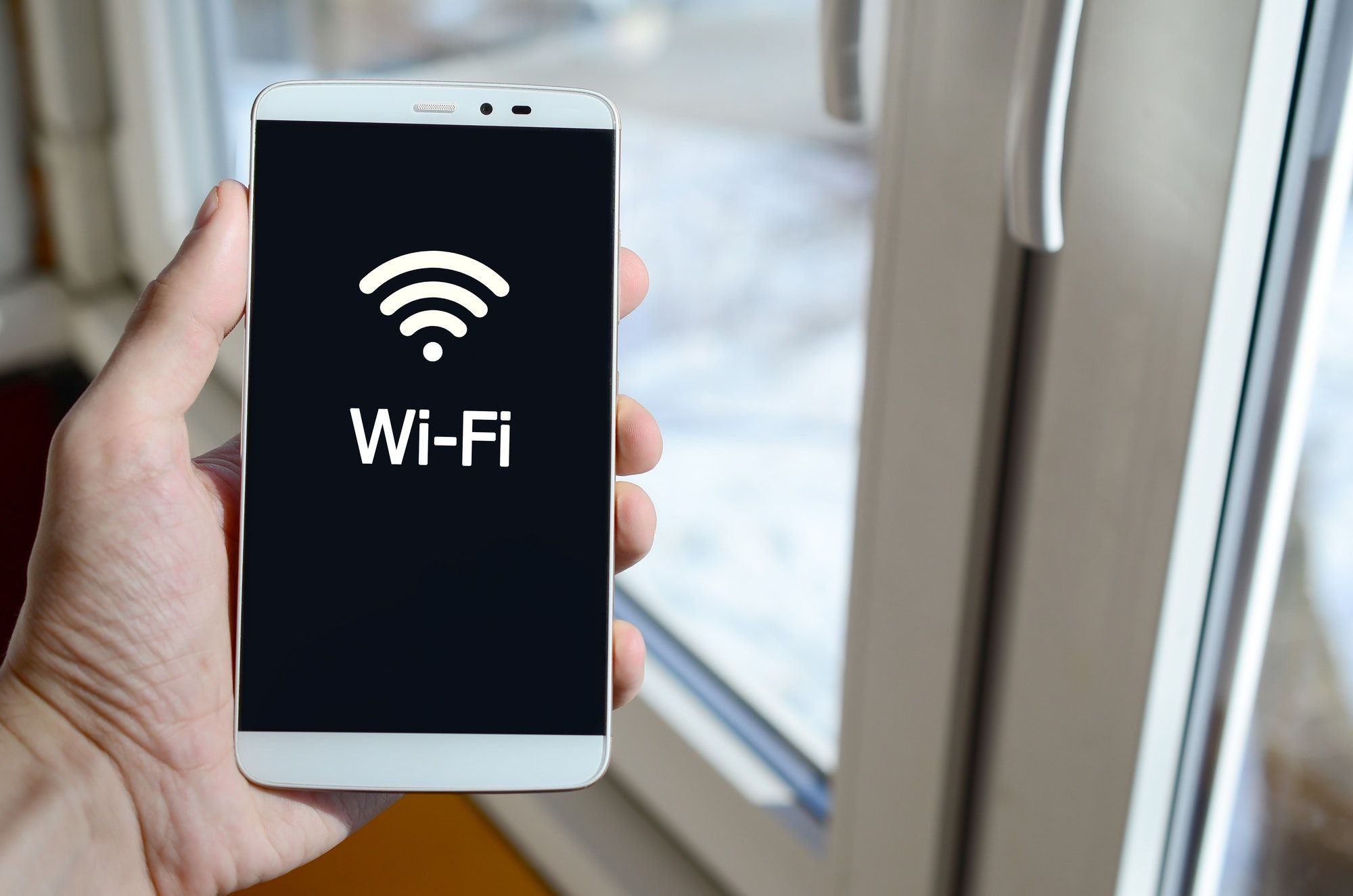 A person sees a white inscription on a black smartphone display that holds in his hand. Wi-Fi